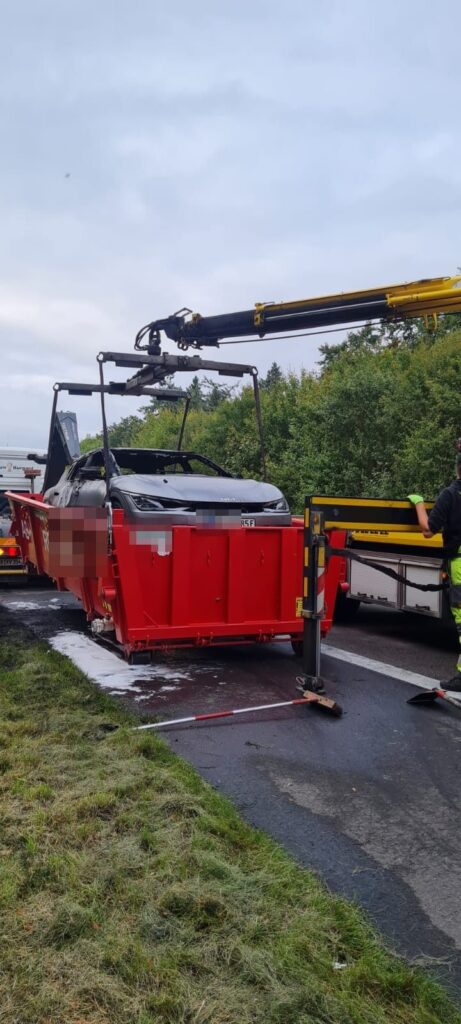 Ein Elektroauto wird an der Autobahn in den Löschcontainer verladen
