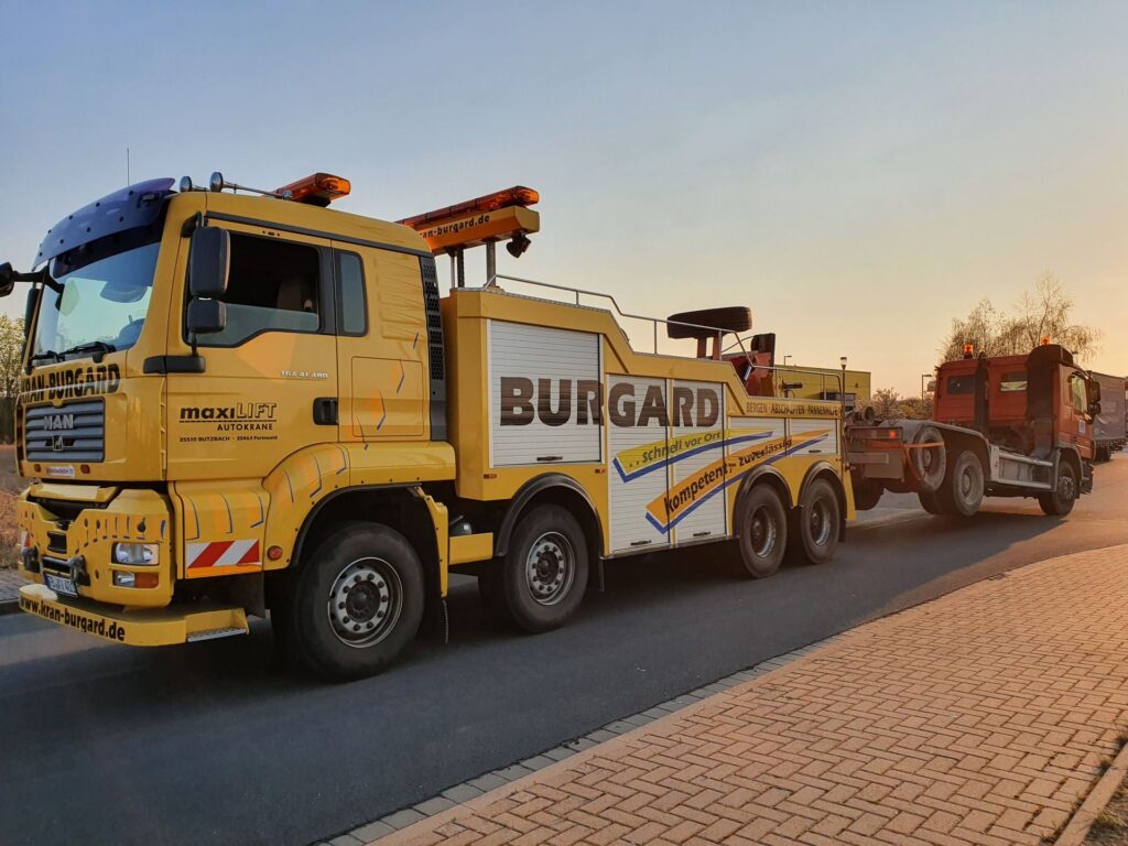 Schweres Bergefahrzeug von Kran-Burgard schleppt einen Lkw im Abendlicht ab
