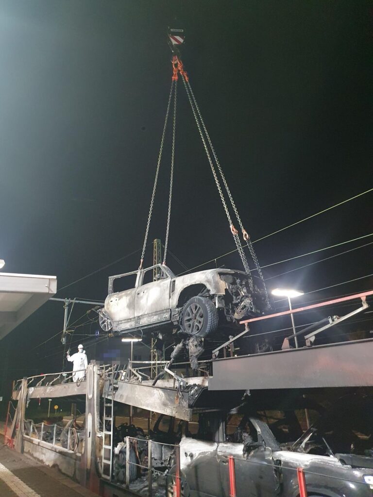 Autokran hebt ein ausgebranntes Fahrzeug nach dem Zugbrand in Butzbach